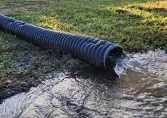 A hose is drained into a puddle on a grassy field.