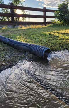 A hose is drained into a puddle on a grassy field.