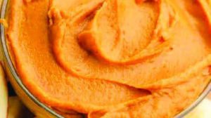 A bowl of pumpkin hummus with apples on a cutting board.