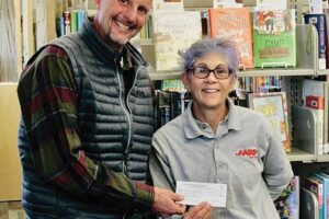 A man and woman standing in front of a bookshelf with a check