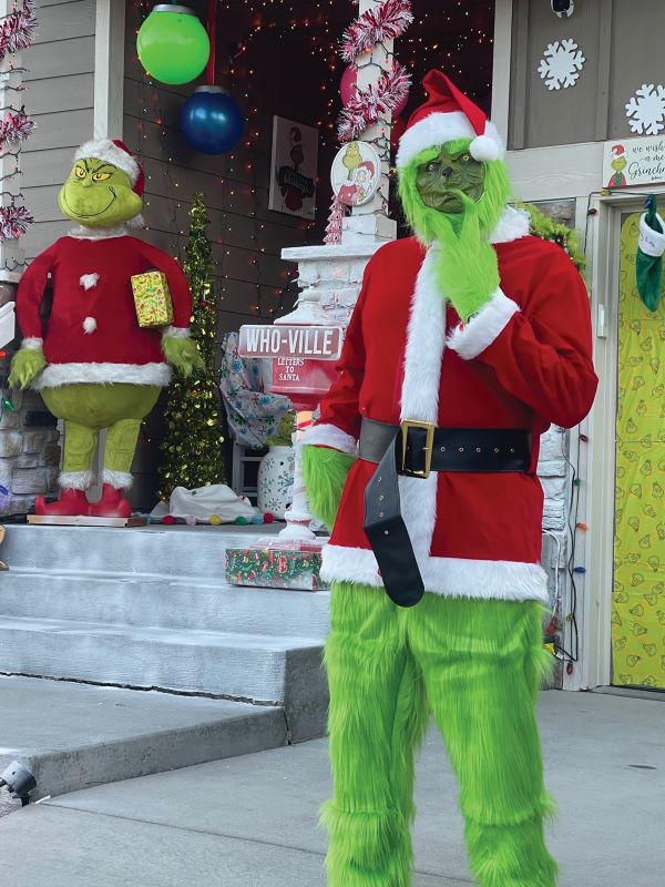 A man dressed in a green santa claus costume is standing in front of a house