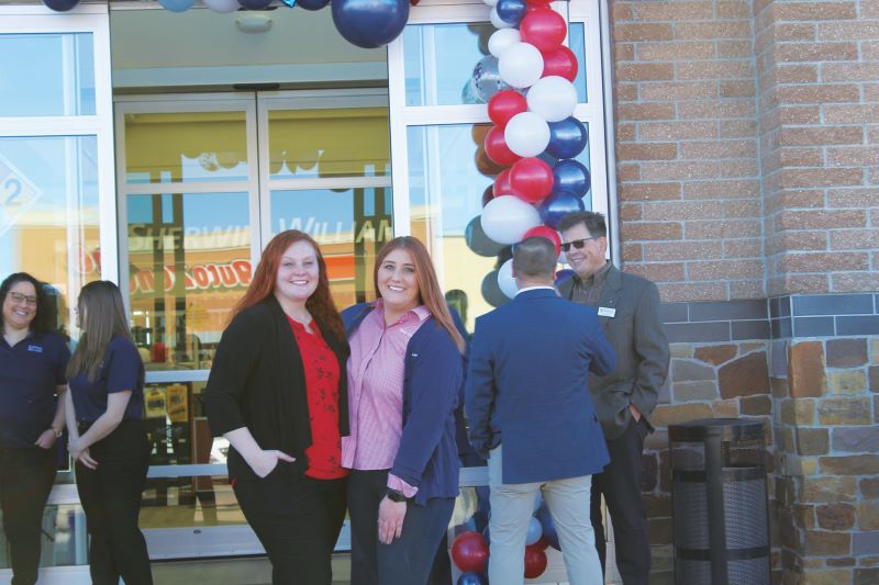 A group of people standing in front of a store with red, white and blue balloons