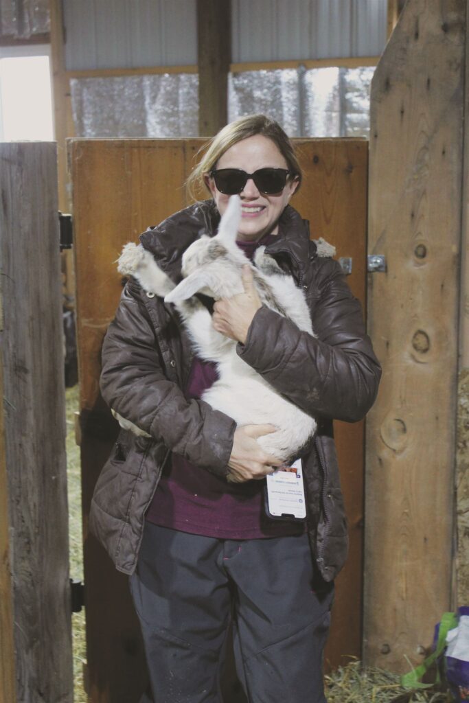 A woman holding a baby goat in a barn