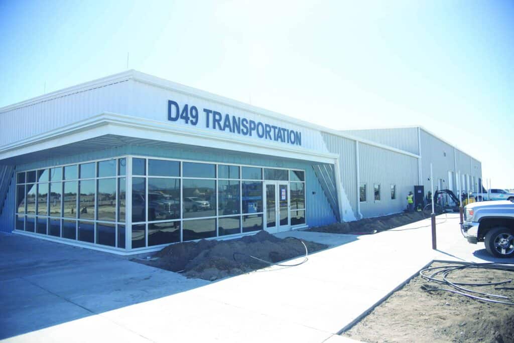 Exterior view of the d49 transportation building with large windows, white walls, and a parked truck on a sunny day.