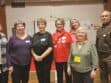 Group of seven adults posing for a photo at an indoor event with name tags.