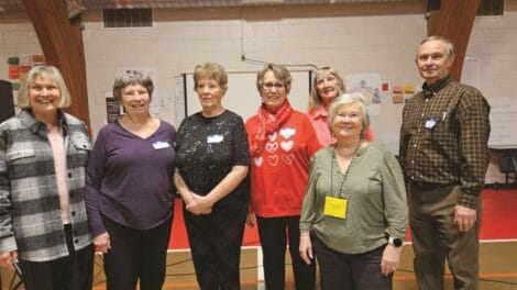 Group of seven adults posing for a photo at an indoor event with name tags.
