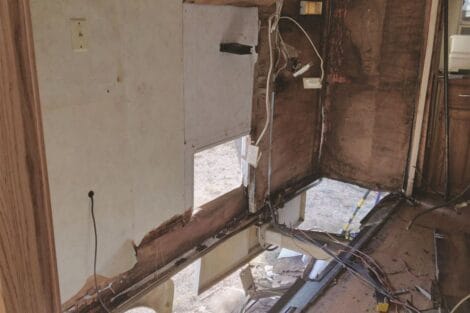 Interior of a dilapidated room with exposed insulation and wiring, and missing wall panels.