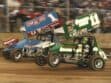 Two sprint cars racing side by side on a dirt track.