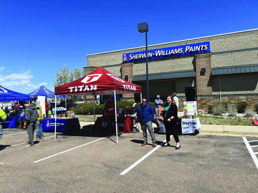 People visiting vendor booths at a local event outside a sherwin-williams paints store under a clear sky.