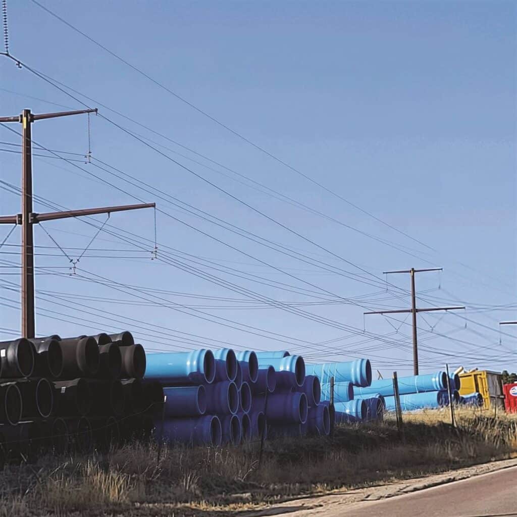 Stacks of blue pipes lined up beside a road with power lines in the background.