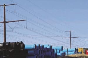 Stacks of blue pipes lined up beside a road with power lines in the background.