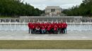 A group of people wearing red jackets poses in front of the world war ii memorial fountains with the lincoln memorial in the background.