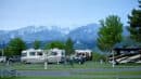 Several motorhomes parked in a campsite with picnic tables in the foreground and snow-capped mountains in the background.