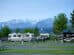 Several motorhomes parked in a campsite with picnic tables in the foreground and snow-capped mountains in the background.