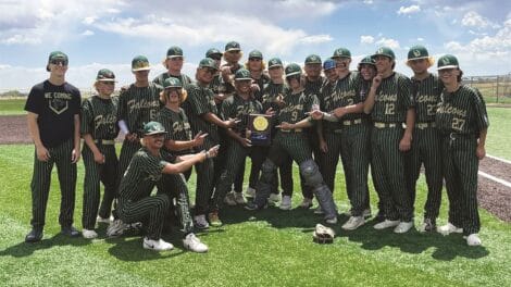 A baseball team in striped black and green uniforms poses on a field with a trophy, pointing at it and smiling.
