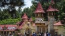 People gather outside a medieval-style castle with red roofs at a Renaissance Festival, surrounded by trees and various stalls.