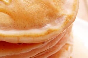 A close-up view of a stack of pancakes topped with a small amount of butter and drizzled with syrup.