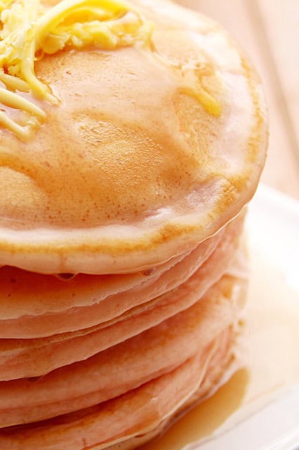 A close-up view of a stack of pancakes topped with a small amount of butter and drizzled with syrup.