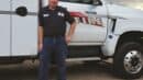 A man in a work uniform stands in front of a Falcon Fire truck equipped with a large crane arm.