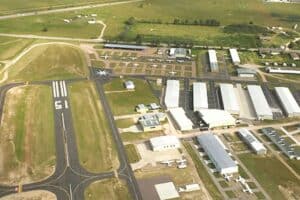 Aerial view of a small airfield with multiple runways, hangars, and parked light aircraft amidst surrounding green fields.