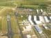 Aerial view of a small airfield with multiple runways, hangars, and parked light aircraft amidst surrounding green fields.