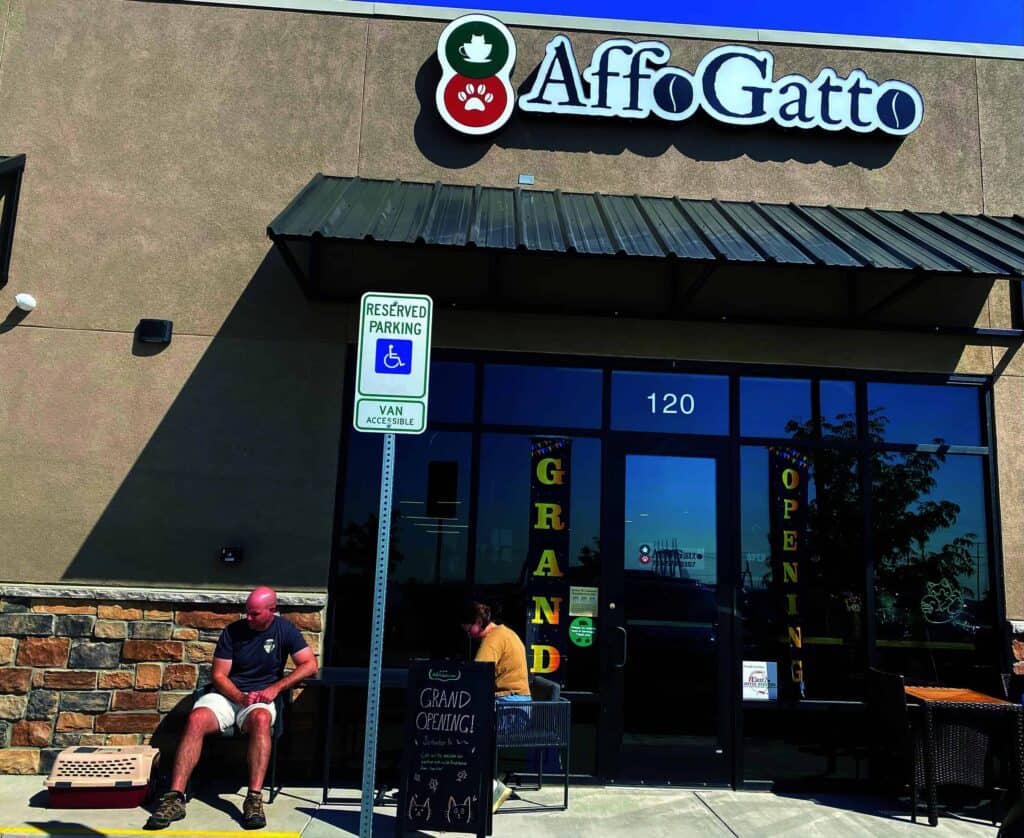 People sitting outside AffoGatto store with "Grand Opening" signs on glass doors. A reserved parking sign is in front.