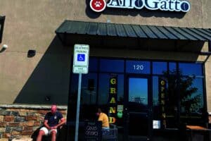 People sitting outside AffoGatto store with "Grand Opening" signs on glass doors. A reserved parking sign is in front.