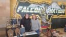 Two women stand behind a jewelry display table in front of a "Falcon Nation" mural.