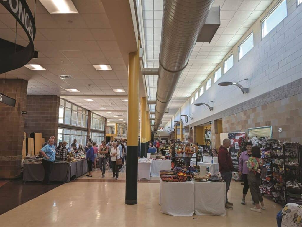 People browsing tables at a craft fair in a large indoor space with high ceilings and natural light.