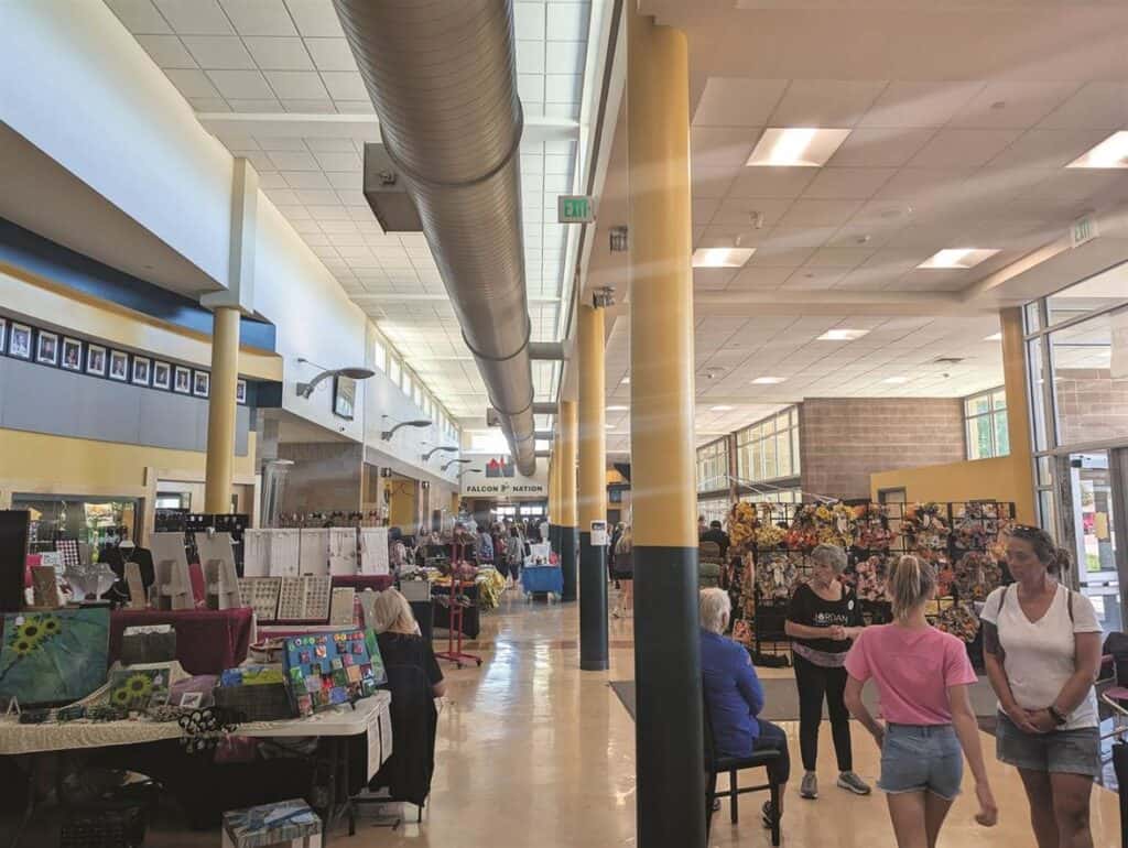 People are browsing various stalls inside a bustling indoor market with high ceilings and bright lighting.