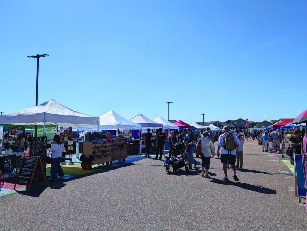 People browsing stalls at an outdoor market with white tents on a clear day.