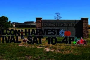 A sign reads "Falcon Harvest Festival Sat 10-4P" in front of Falcon High School, with fall-themed decorations on a grassy area.