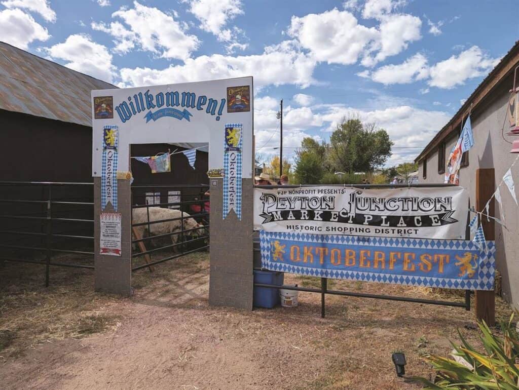 Entrance to an outdoor area with a "Willkommen" sign, Oktoberfest banners, and a Peyton Junction Mare & Placy shopping district sign.