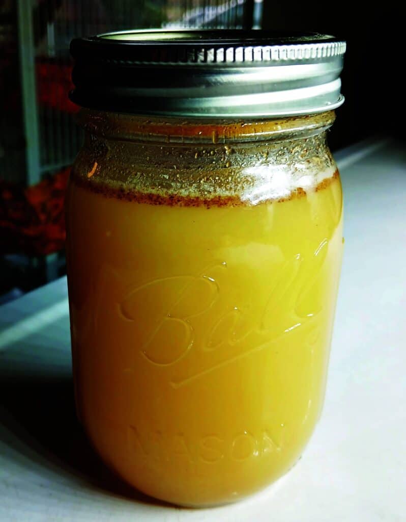 A mason jar filled with a creamy yellow liquid, sealed with a metal lid, sitting on a white surface.