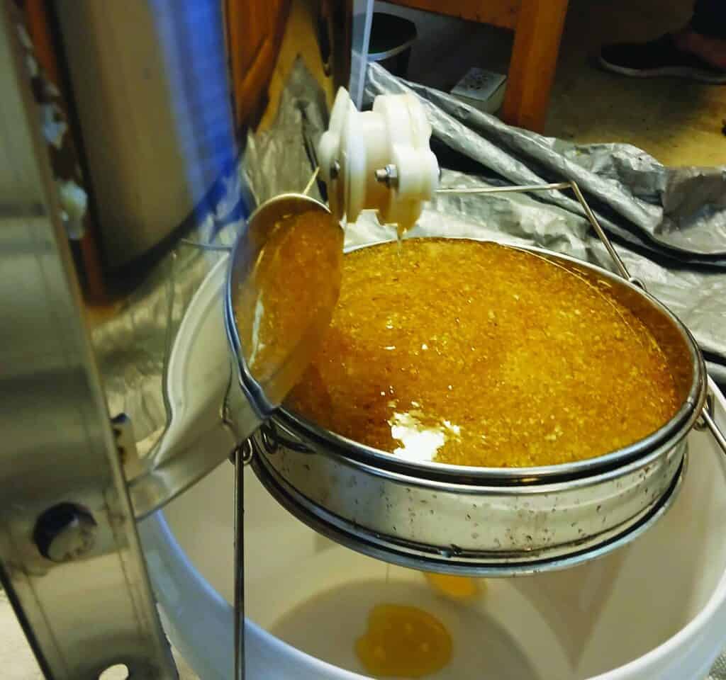 A honey extractor spins honey from combs, dripping into a bucket below.