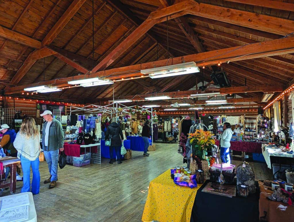 A rustic indoor market with wooden beams, tables displaying various items, and people browsing.