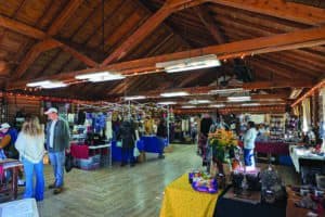 A rustic indoor market with wooden beams, tables displaying various items, and people browsing.