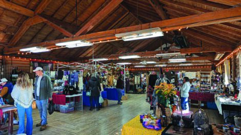 A rustic indoor market with wooden beams, tables displaying various items, and people browsing.