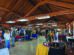 A rustic indoor market with wooden beams, tables displaying various items, and people browsing.