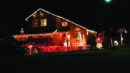 House decorated with red and white Christmas lights, a "Candy Cane Lane" sign, and festive figures like snowmen and Santa at night.