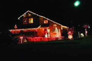 House decorated with red and white Christmas lights, a "Candy Cane Lane" sign, and festive figures like snowmen and Santa at night.