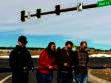 Four people stand holding scissors, cutting a blue ribbon at a road intersection with traffic lights and a street sign labeled "Rex Rd.