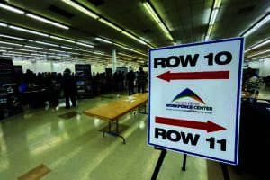 Job fair with booths set up in a large room. A sign points to Rows 10 and 11, labeled "Pikes Peak Workforce Center." People are visible in the background exploring the event.