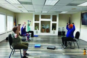 Three people are seated on chairs in a room, lifting weights as part of an exercise session.