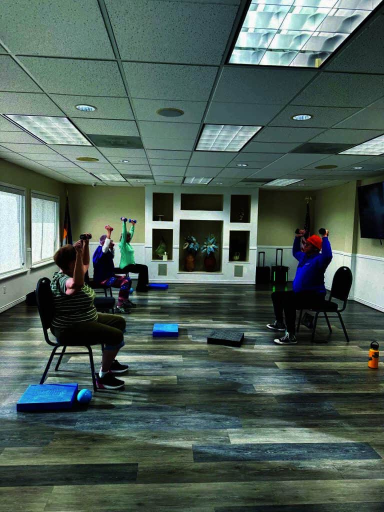 Three people are seated on chairs in a room, lifting weights as part of an exercise session.