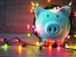 A white piggy bank wrapped in colorful string lights on a wooden surface.