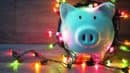 A white piggy bank wrapped in colorful string lights on a wooden surface.