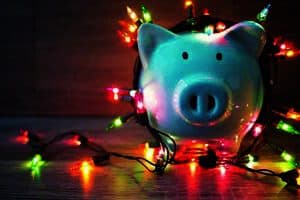 A white piggy bank wrapped in colorful string lights on a wooden surface.