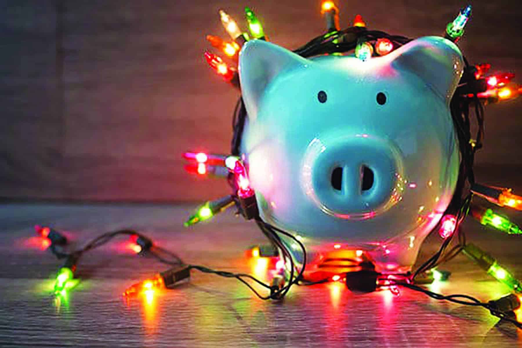 A white piggy bank wrapped in colorful string lights on a wooden surface.