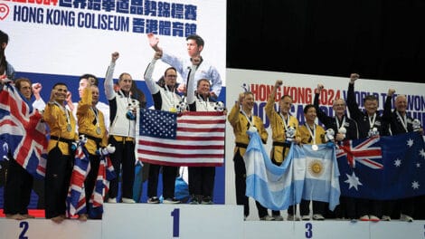Group of medalists on a podium at a martial arts tournament. They are holding flags and plush toys, celebrating their victories.